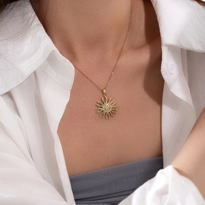 Detail of sun pendant necklace in gold finish worn with white shirt for women