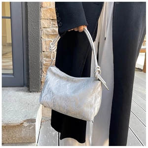 Detail of silver pleated shoulder bag featuring unique knotted strap design and soft texture