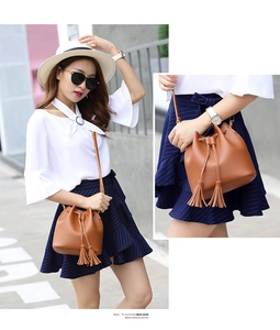 Detail view of brown faux leather bucket bag with tassels and drawstring closure on model