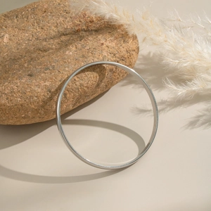 Polished stainless steel bangle displayed against natural stone for a minimalist aesthetic