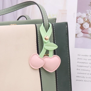 Macro shot of pink heart-shaped cherry charm with green leaves on a tote bag handle