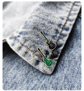 Close-up of black and green electric guitar enamel pins on a denim jacket lapel