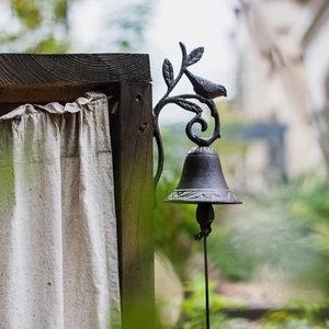 Vintage cast iron garden doorbell with bird and leaf details on a rustic wooden post