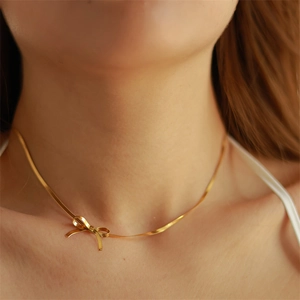 Close-up of gold bow pendant on a delicate snake chain necklace worn by a model