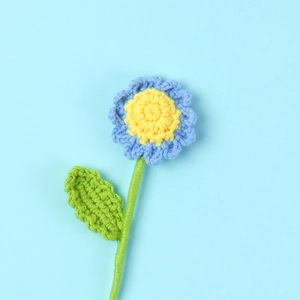 Detail of handmade crochet daisy with blue petals and yellow center on blue background