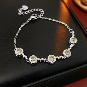 Detail of silver bracelet with five round green zircons on a black leather surface