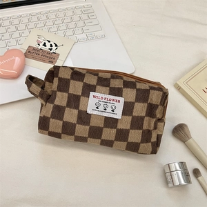 Close-up of checkerboard corduroy makeup bag with secure zipper and handle on a desk