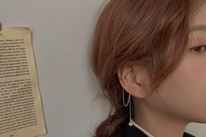 Close-up of silver tassel ear cuff with layered rings and a pearl drop on a model