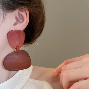 Close-up of large irregular geometric acrylic earrings in deep reddish-brown color
