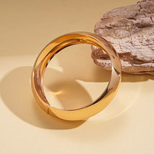 Primo piano di un bracciale rigido dorato lucido minimalista su un blocco di legno