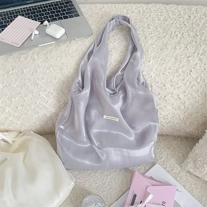 Flat lay of a glossy lavender satin tote bag with modern lifestyle accessories on plush rug