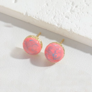 Detail of round gold earrings with pink and blue marbled resin finish on white stone