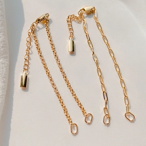 Makro-Detail von goldenen Paperclip-Verlängerungsketten mit Karabinern und Metallanhängern