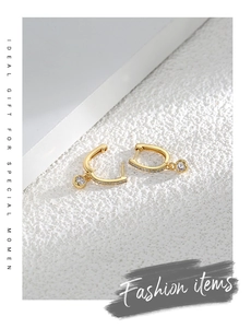 Detail of gold-plated U-shaped earrings with micro-set zircon stones on white surface