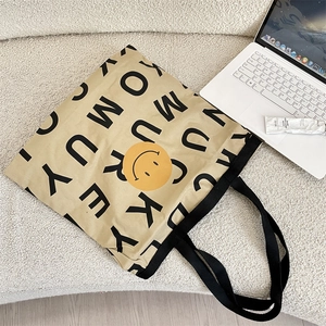 Detail shot of the canvas tote bag showing black letter prints and a yellow smiley face