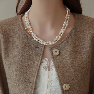 Gros plan d'un collier de perles double rang avec fermoir doré porté avec un manteau en laine