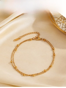 Detail einer goldenen doppellagigen Perlenkette am Fuß auf weichem beige Seidenstoff