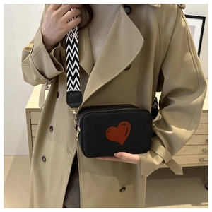 Detail of black crossbody camera bag with red heart accent and wide geometric strap