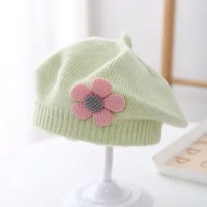 Close-up of a mint green knitted baby beret with a pink flower and ribbed trim detail