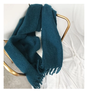 Close-up of soft thick dark teal knit scarf with fringe detail draped on a golden chair