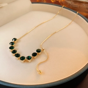 Dettaglio macro di una collana placcata in oro con nove pietre verde smeraldo su velluto