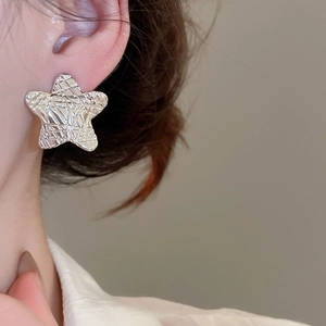 Close-up of silver star stud earring with embossed hammered texture on model's ear