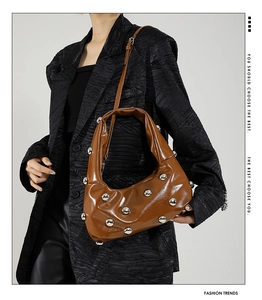 Close-up of brown leather bag with silver rivets held by a model in a black blazer
