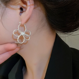 Close-up of silver hollow five-petal flower earring with pearl on model's ear