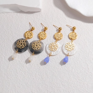 Elegant gold drop earrings with marble disc and floral accent on textured background