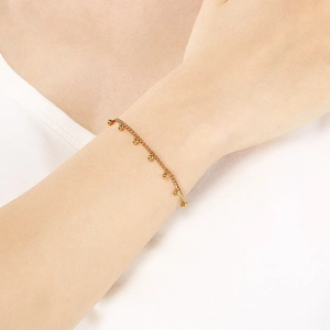 Close-up of gold beaded chain bracelet worn by a model against a soft white outfit