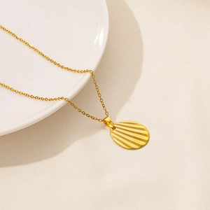 Detail of a vintage 18k gold-plated oval pendant with radial texture on a white plate
