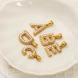 18k gold plated stainless steel letter charms A-D with pearls in a white ceramic dish