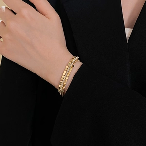 Détail d'un bracelet géométrique doré avec paillettes et diamants sur fond de manche noire
