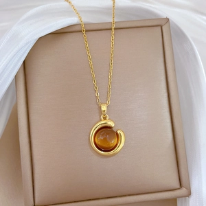 Macro shot of gold necklace featuring a round amber gemstone pendant on silk background
