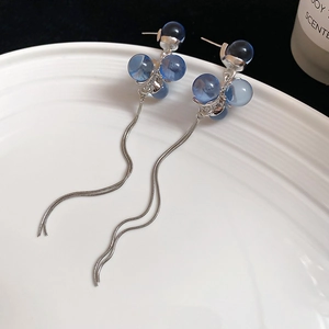 Detail shot of long silver tassel earrings with blue resin beads on a white tray