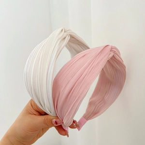 Close-up of pleated fabric headbands in beige and pink with twisted knot design