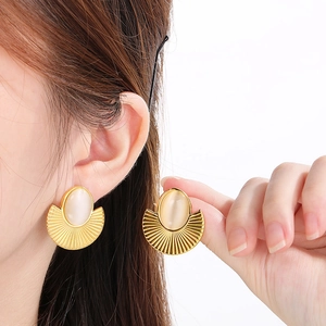 Close-up of golden fan-shaped earrings with oval cat-eye stones shown on a model