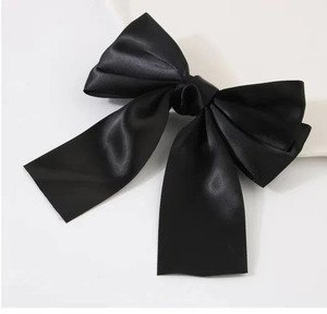 Close-up of a smooth black satin bow hair clip with elegant hanging ribbons on white background