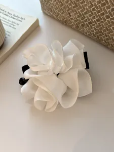 Détail de la pince à cheveux en organza blanc avec base noire sur fond crème élégant