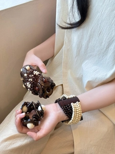 Detail of bohemian wood and coconut shell beaded bracelets on female wrist with earthy tones