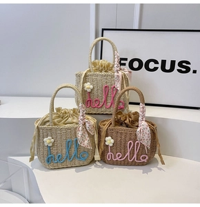Detail of handmade woven straw bags featuring daisy flowers and 'hello' embroidery