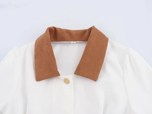 Detail of white corduroy dress featuring a brown lapel collar and a gold button