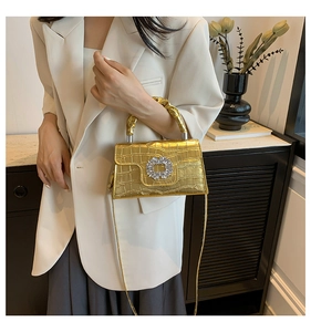 Close-up of golden croc-embossed handbag featuring a crystal buckle and twisted handle