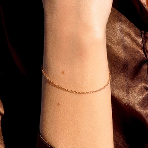 Close-up of minimalist rose gold fine chain bracelet on wrist over brown silk background