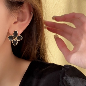 Détail d'une boucle d'oreille fleur en émail noir avec bordure dorée sur un mannequin