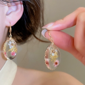 Primer plano de elegantes pendientes de resina artesanales con flores secas reales.