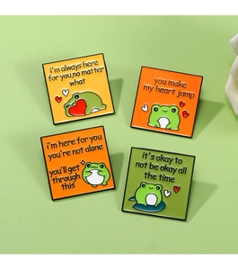 Detailed view of four colorful enamel frog badges with inspiring English quotes on green background
