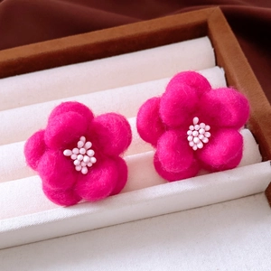 Macro detail of pink felt flower earrings with white bead center in a jewelry box