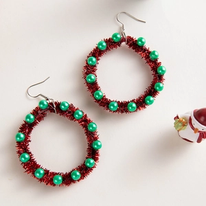 Detail of Christmas wreath earrings with red tinsel and green pearls on white background