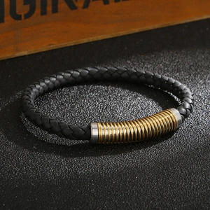 Macro shot of black woven leather bracelet with gold and silver steel coils on wood